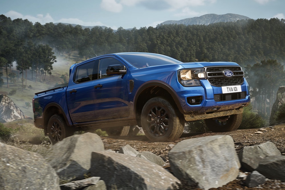 Un Ford Ranger pick-up albastru merge de-a lungul unui drum de pământ dintr-o pădure, lăsând o dâră de praf.