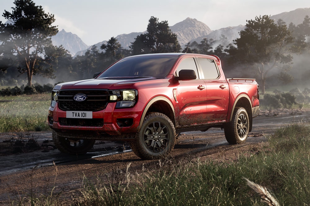 Un Ford Ranger Raptor roșu care se deplasează pe un drum de pământ printr-un peisaj pitoresc.