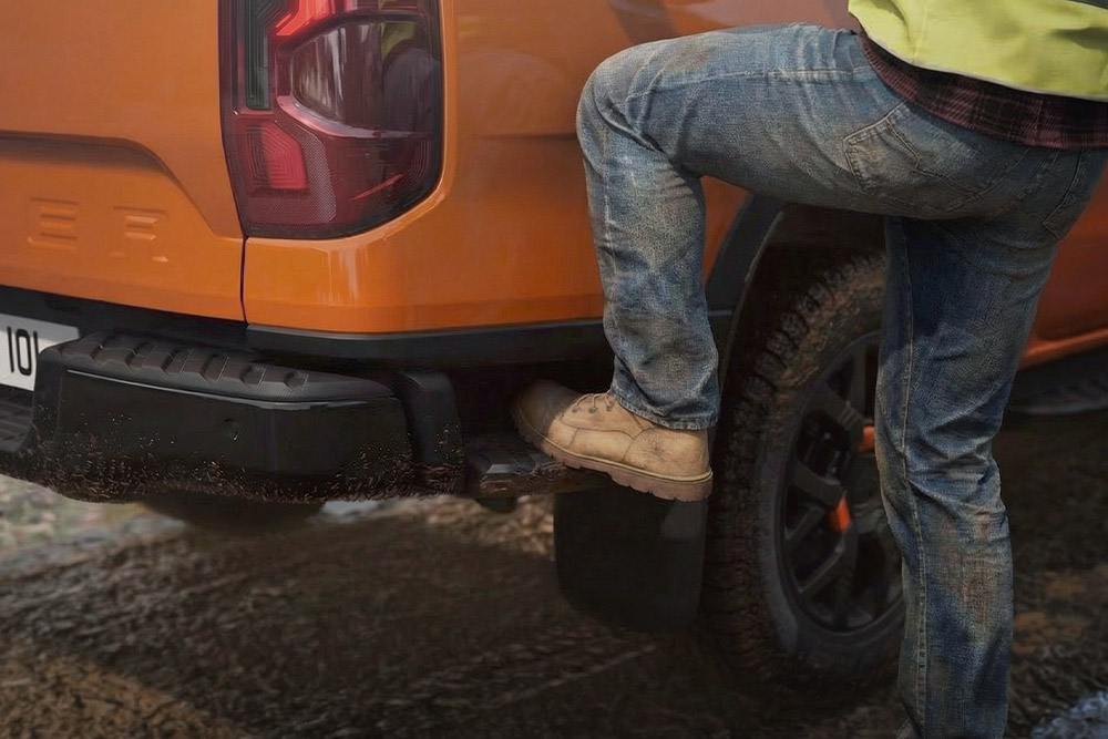 Lucrător care pășește pe treapta din spate integrată a unui Ford Ranger Wildtrak.