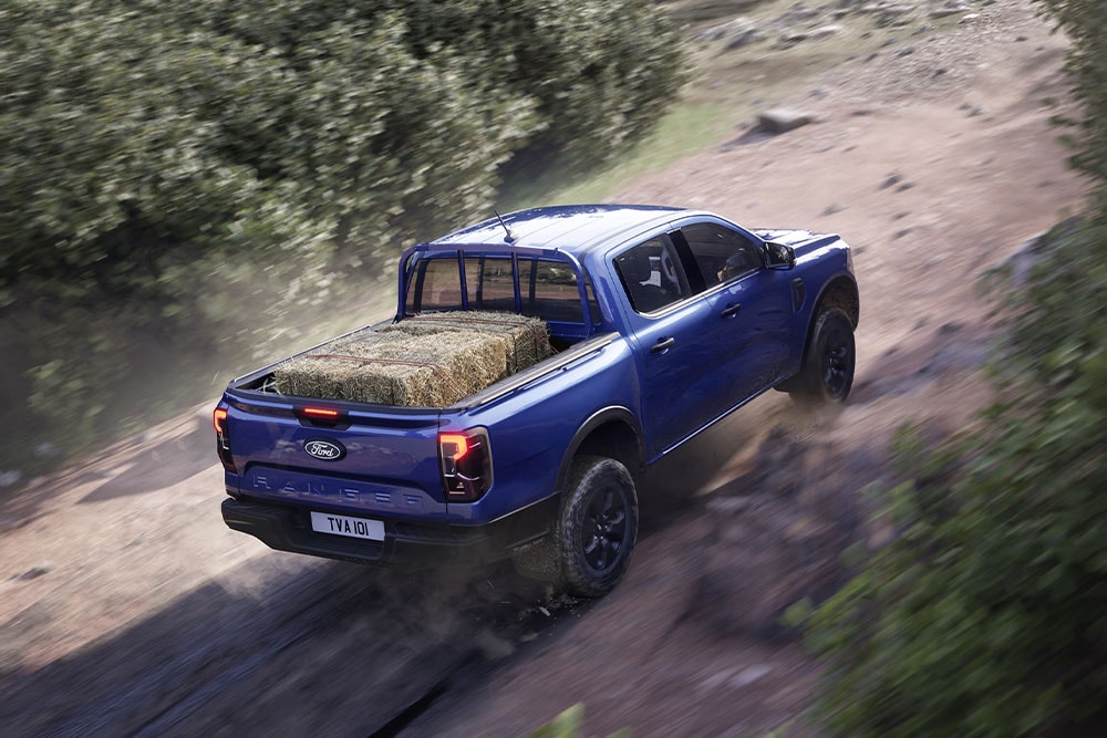 Vedere din spate de sus a unui Ford Ranger albastru care se deplasează pe un drum de pământ.