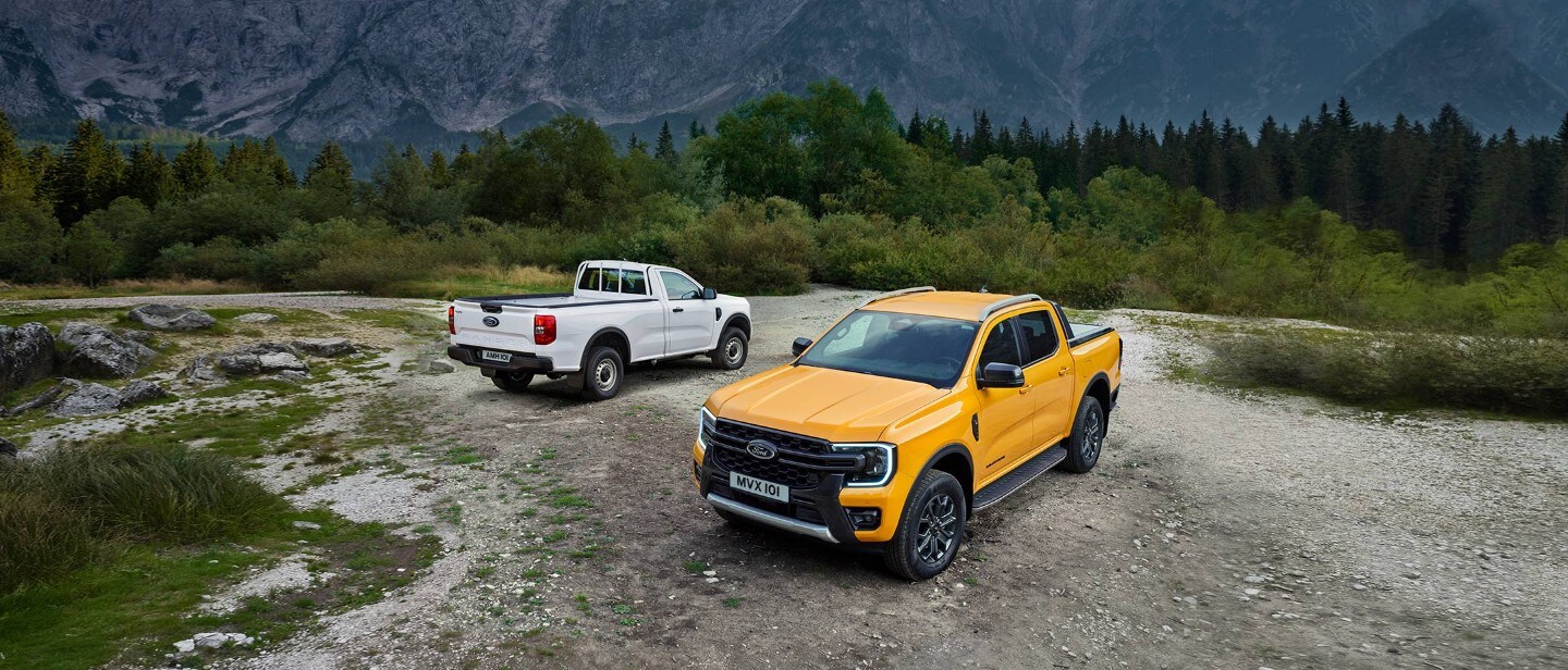 Ford Ranger portocaliu vedere din față 3/4, pe pietriș în fața unui Ford Ranger alb, vedere din spate 3/4