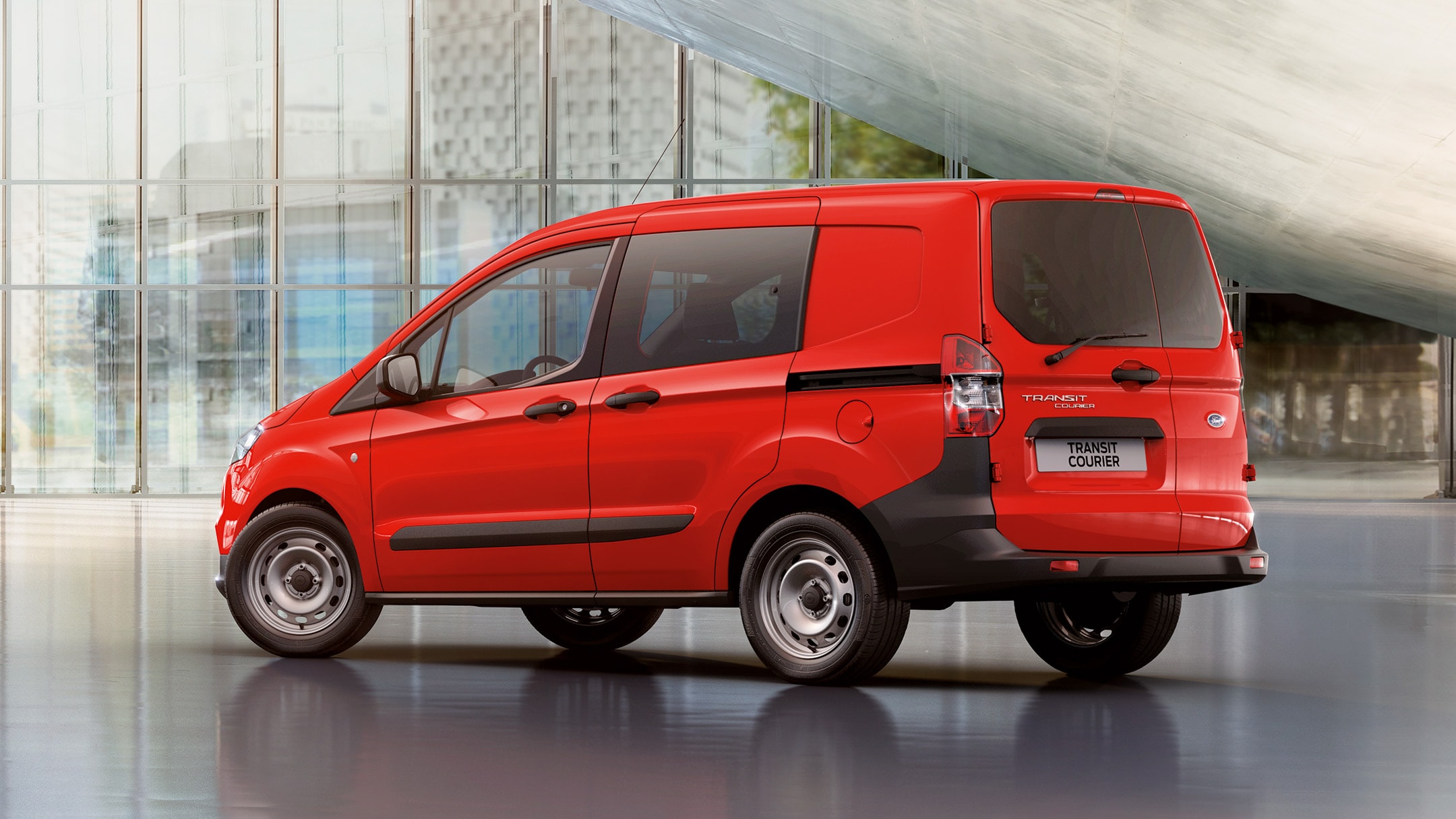 Red Ford Transit Courier standing in front of glass building in side view