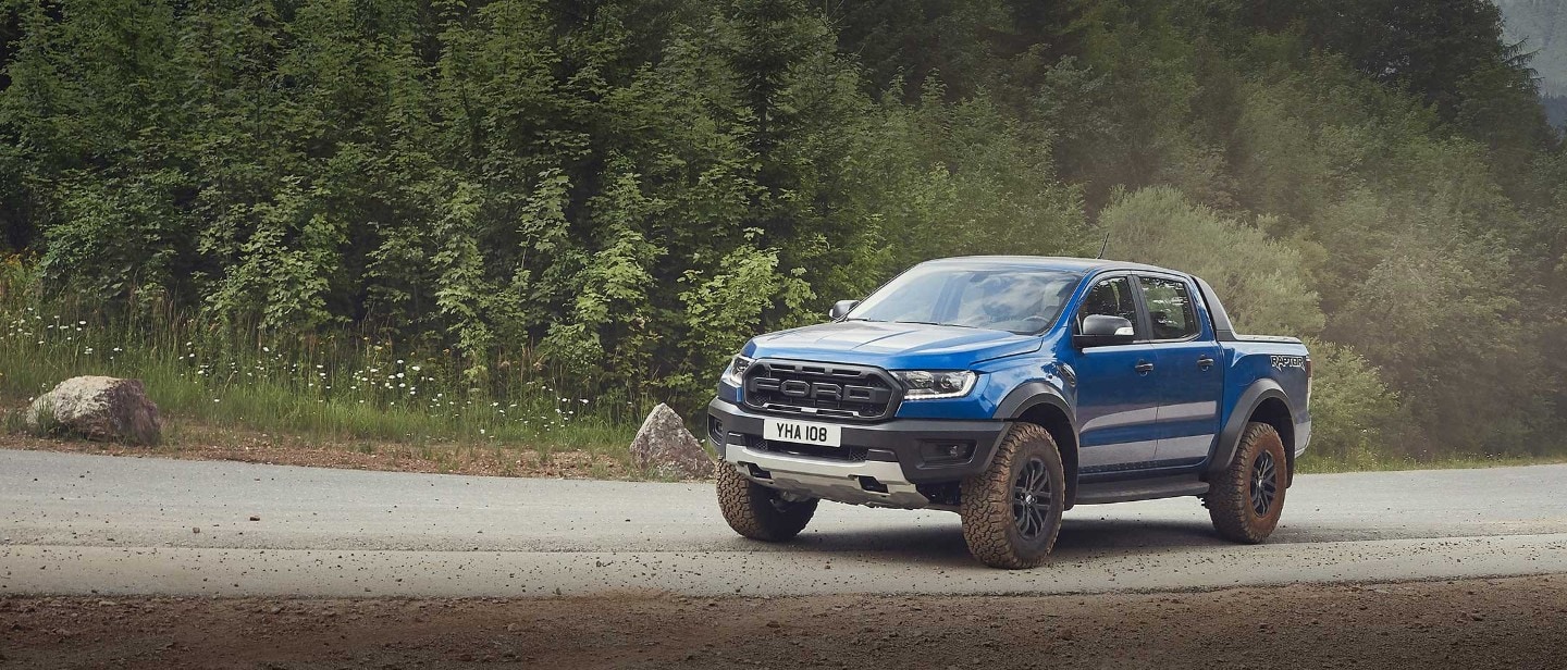 Blue Ford Ranger Raptor driving through a countryside, front three quarter view