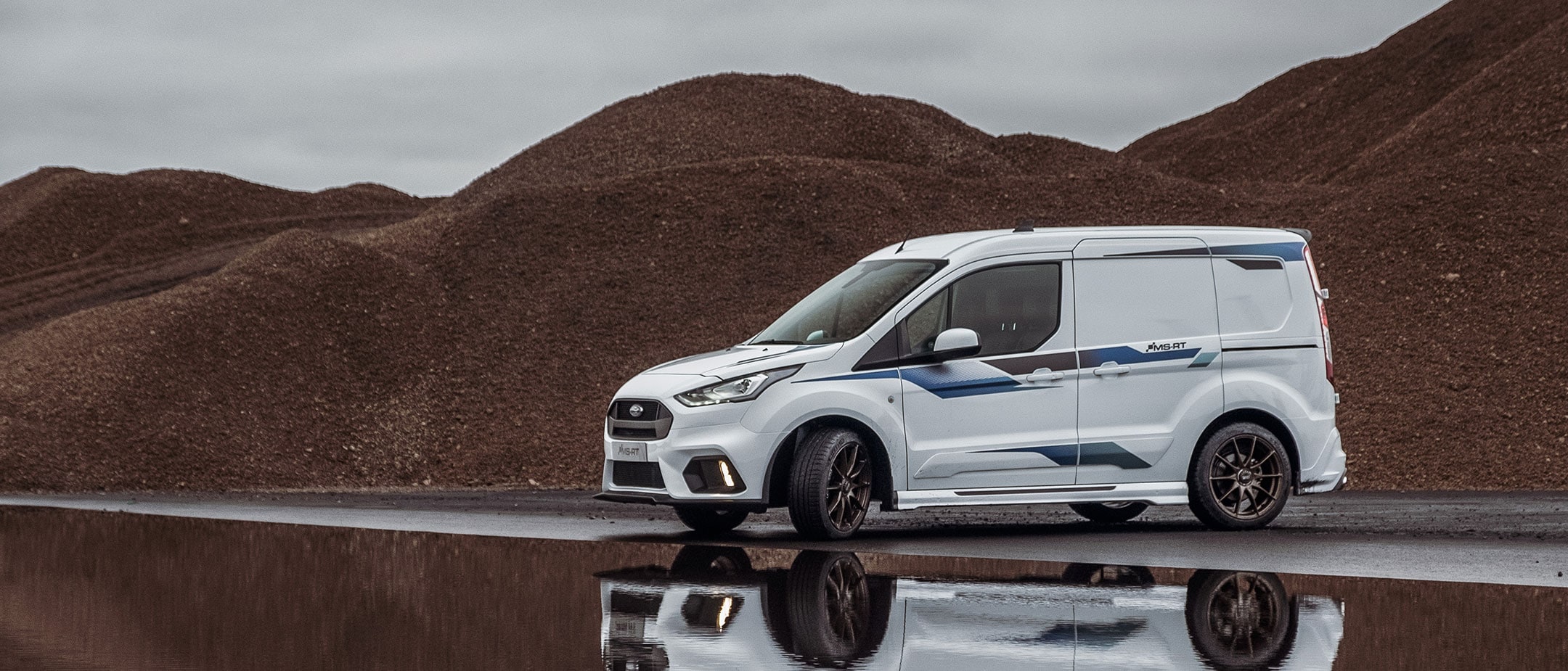 Ford Transit Connect MS-RT parked next to large rubble piles. 