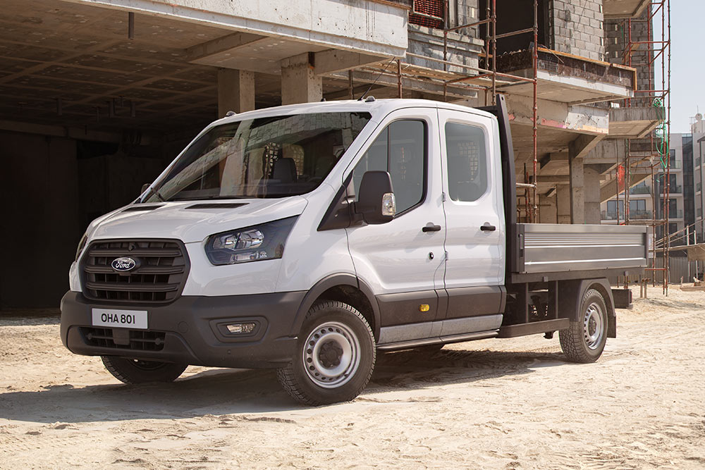  Un Ford Transit Custom alb cu șasiu-cabină și platformă este parcat pe un șantier.