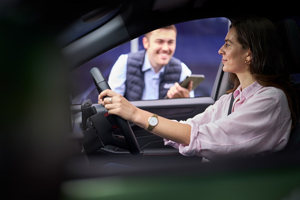 O persoană aflată pe scaunul șoferului unei mașini Ford, privind un tehnician care stă afară și ține o tabletă.