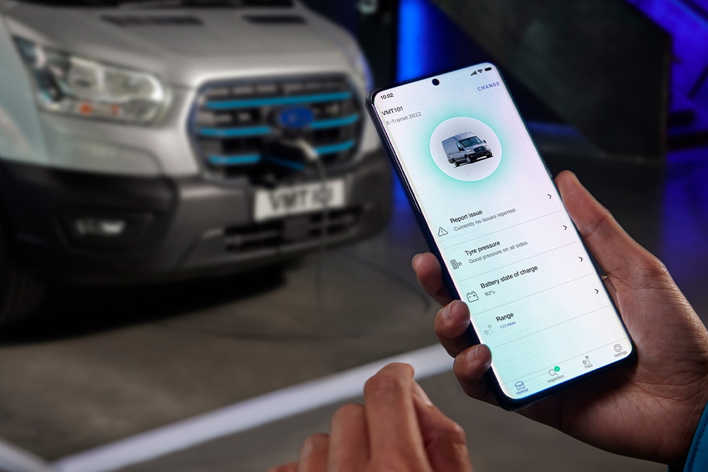 O persoană ține un smartphone cu o aplicație Ford, cu un Ford E-Transit Custom încărcându-se în fundal.