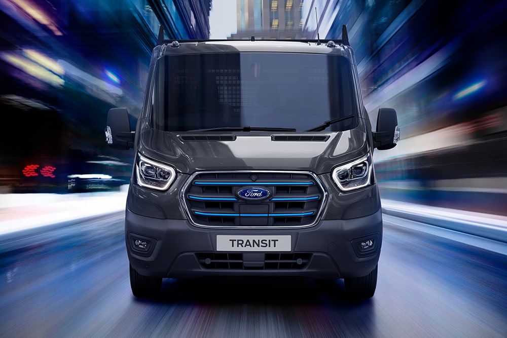 Vedere frontală a unei furgonete Ford Transit gri închis în mișcare, cu un fundal estompat.