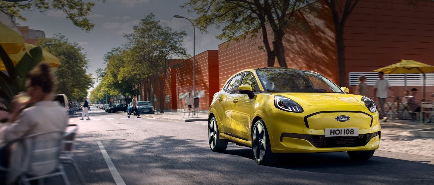 Vedere frontală a unui model Ford Puma Gen-E® electric, de culoare galben, care circulă pe o stradă dintr-un oraș.