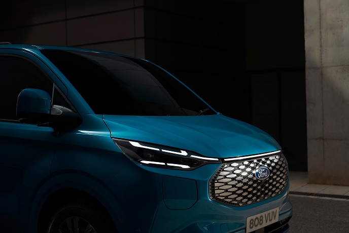 Un prim-plan cu farul unei camionete Ford E-Transit Custom albastre.