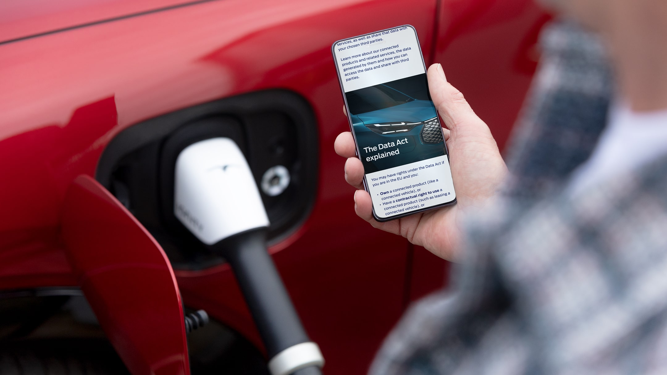 O persoană care citește un document explicativ legat de Actul UE privind datele pe telefonul său lângă un vehicul electric care se încarcă.