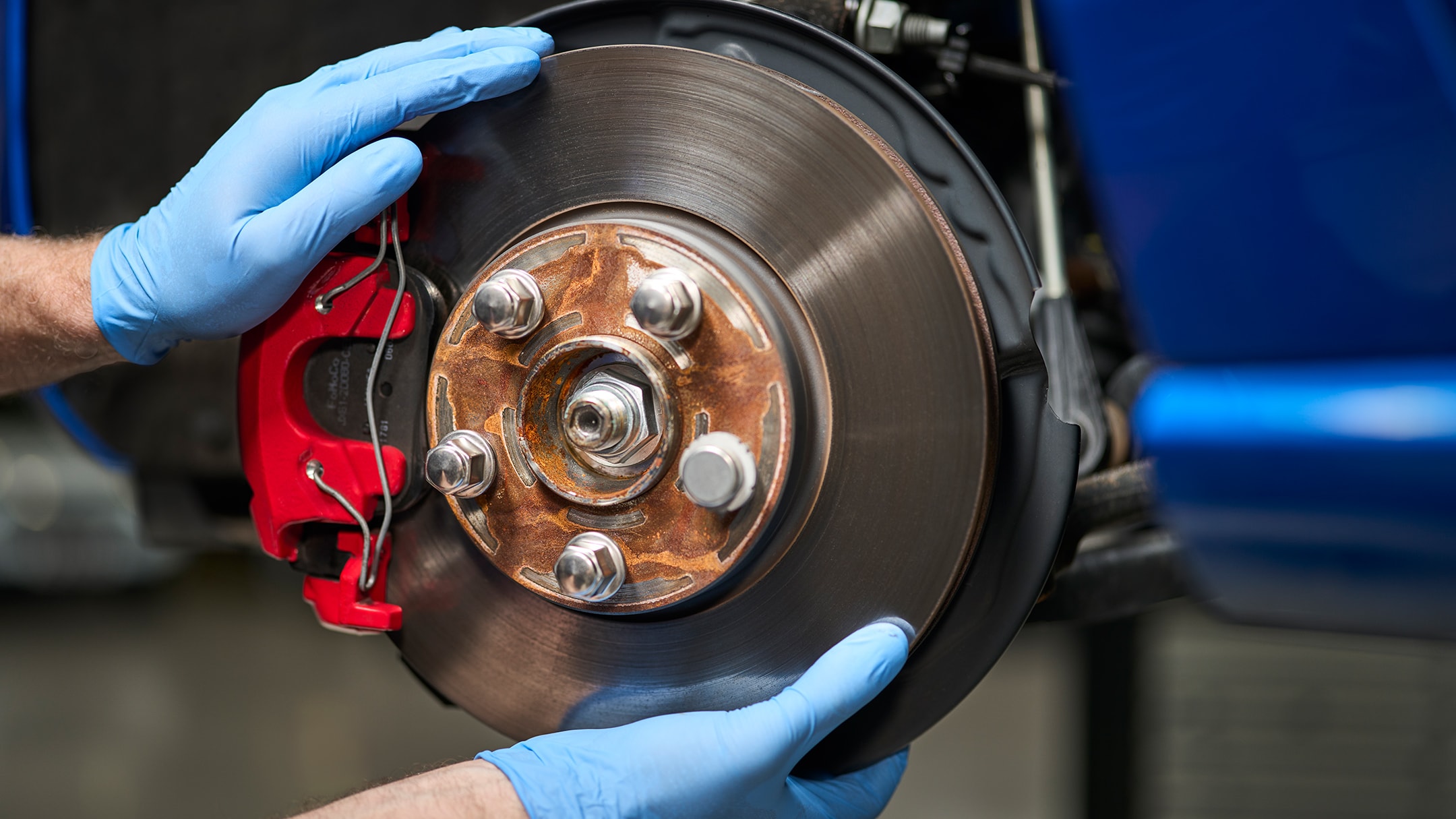 A mechanic wearing blue gloves installs a new brake rotor on a blue car.