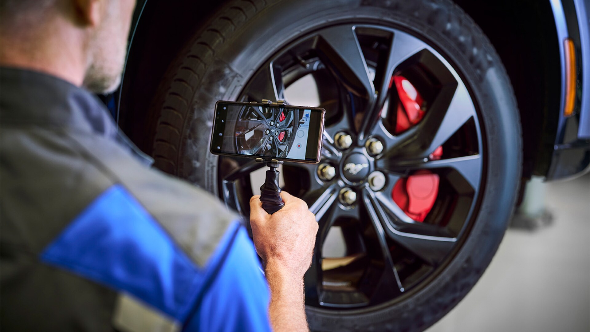 Technician photographing a car wheel and brake assembly.
