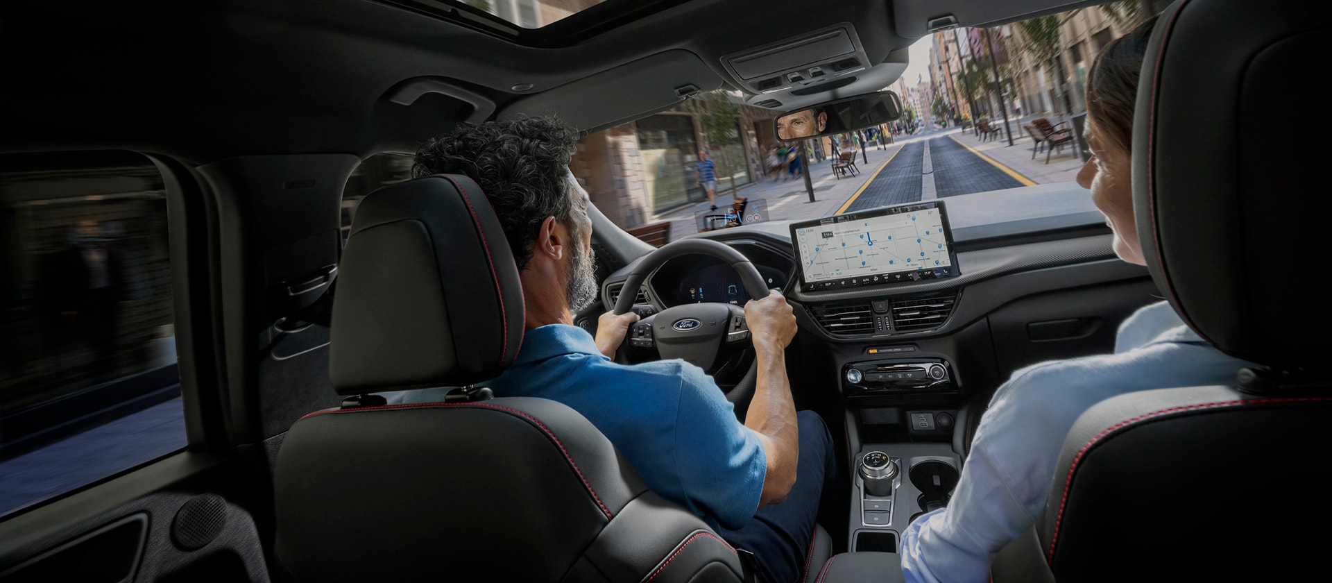 Pasageri într-un vehicul Ford cu ecranul digital SYNC afișat pentru a-i ajuta să navigheze pe un traseu urban.