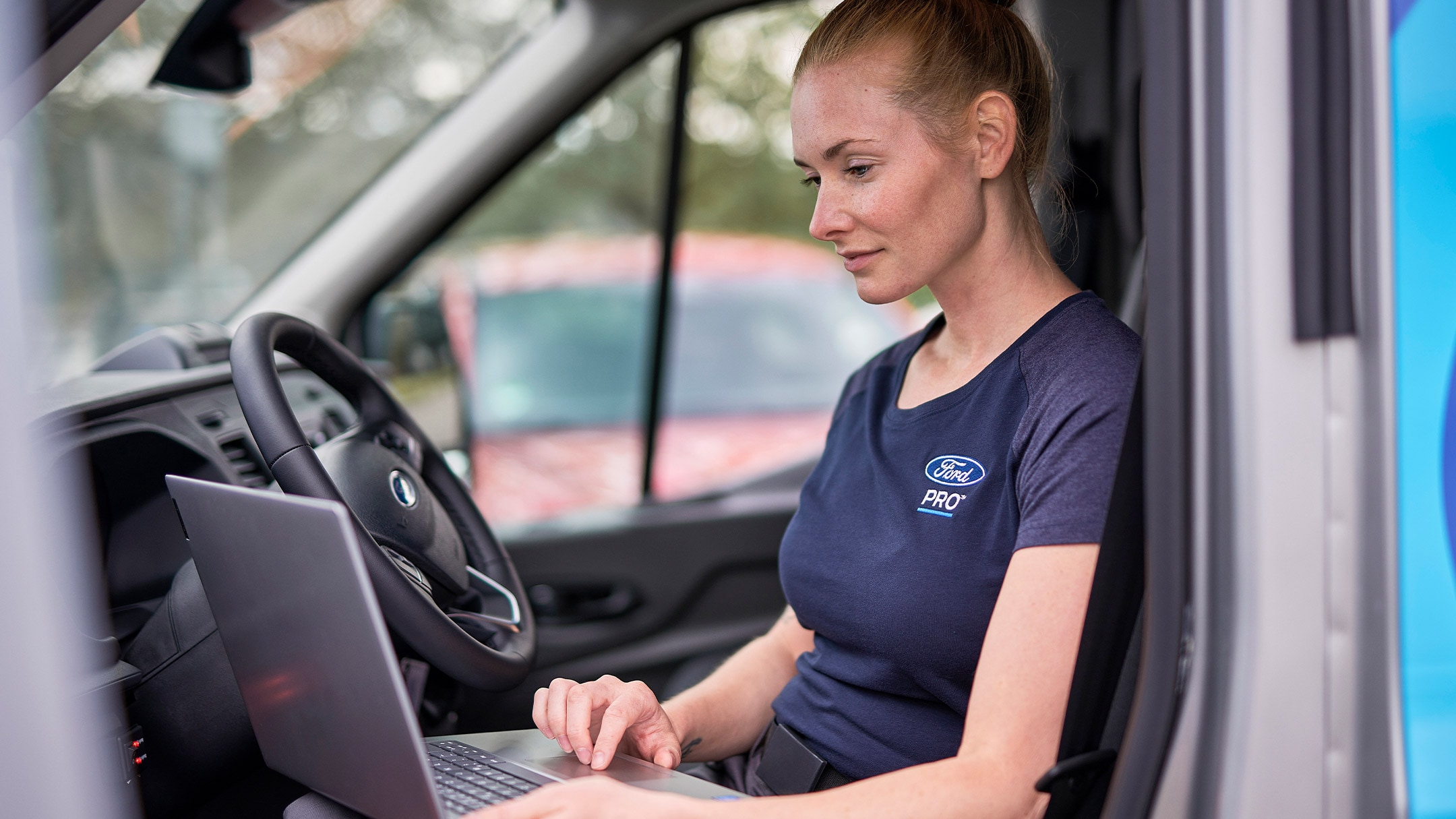 Un expert Ford Pro stă într-o mașină verificând un laptop în timpul unei revizii la vehiculul Ford.