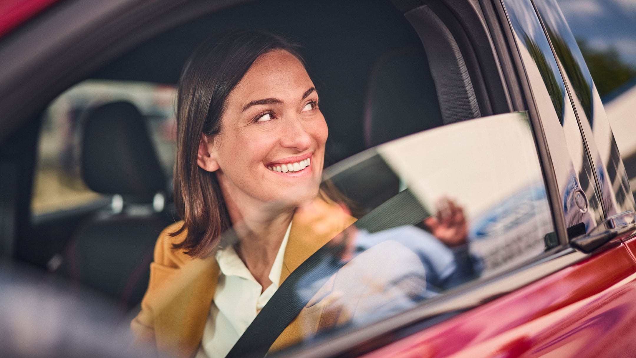 O persoană zâmbește în timp ce stă într-o mașină Ford roșie.