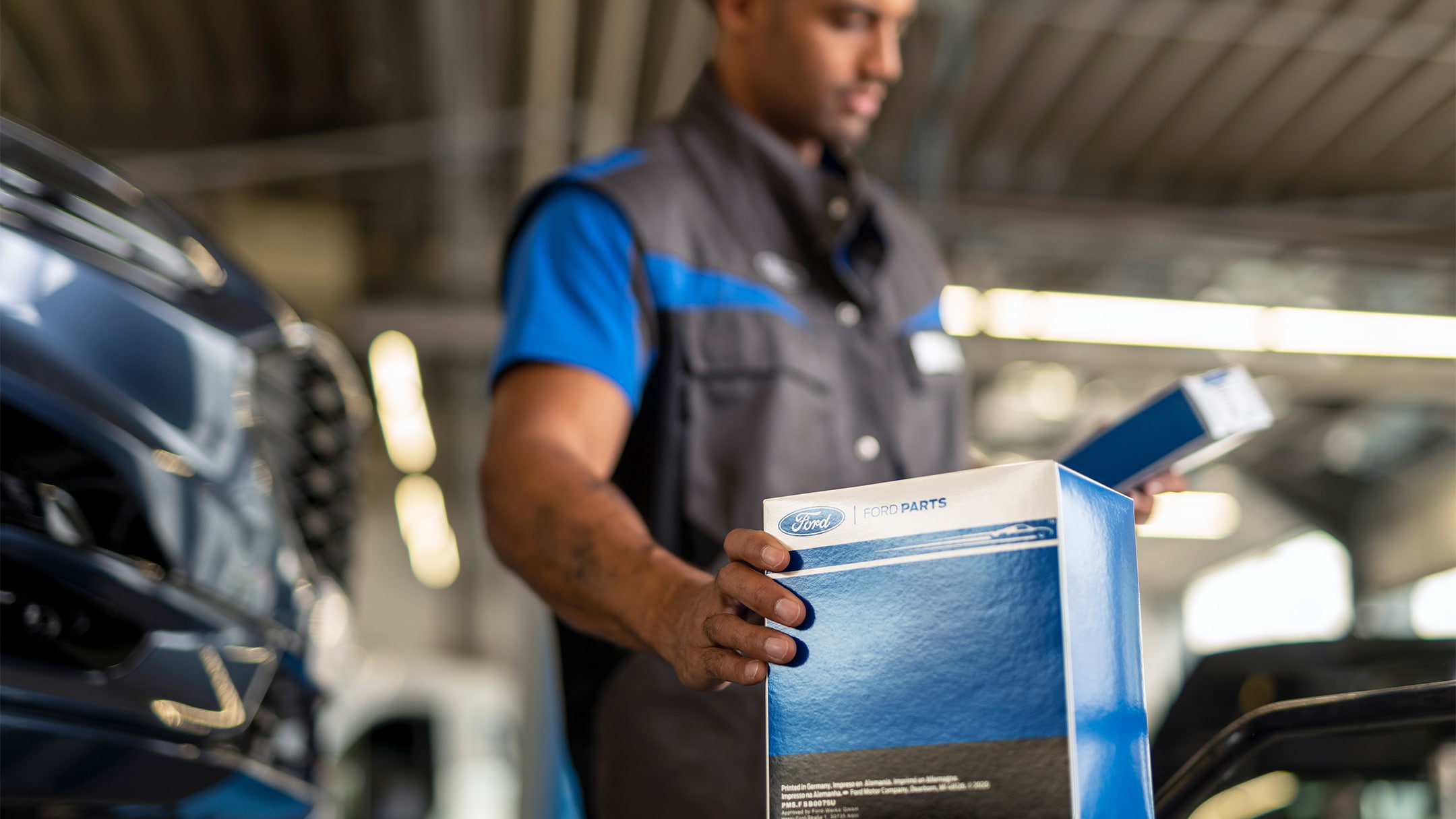 Un mecanic la un centru de service Ford ține în mână o piesă originală Ford ambalată într-o cutie cu sigla sa.