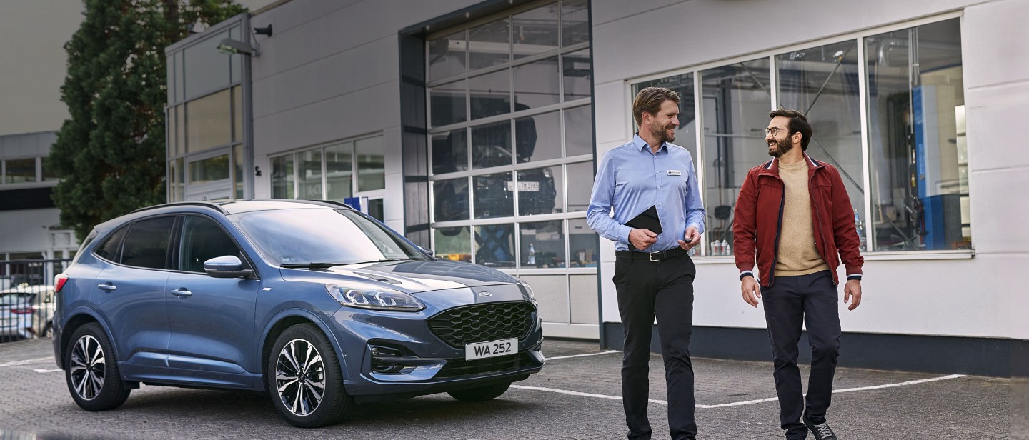 Service employee and customer standing under the car at workshop