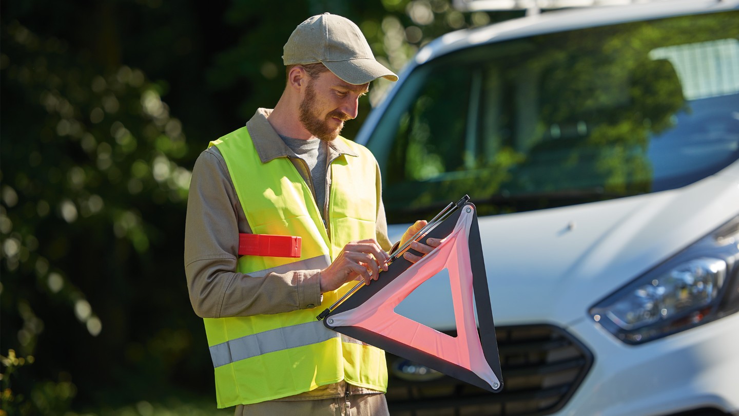 Person in high-visibility vest setting up a warning triangle