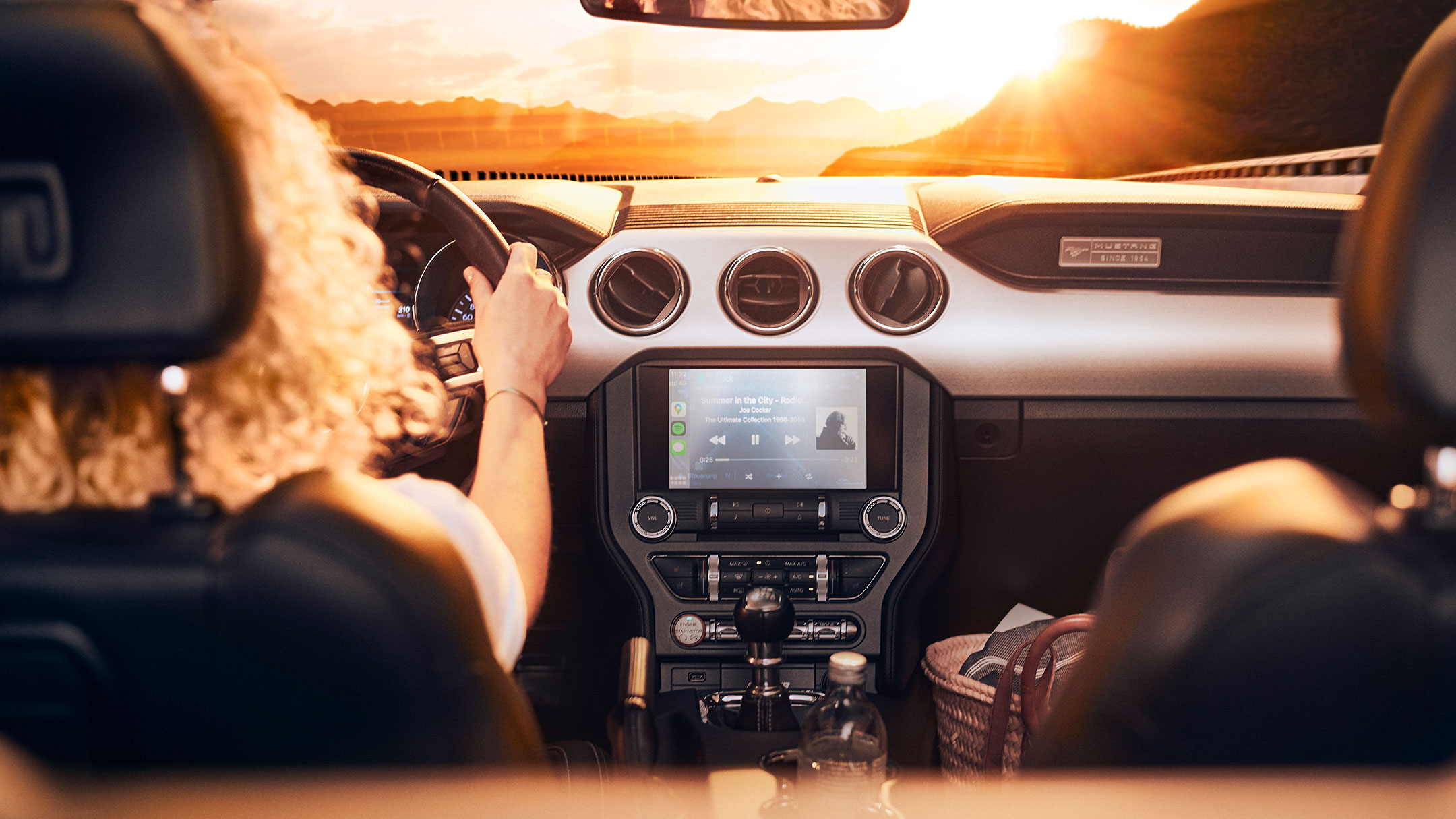 Femeie la volanul unei mașini Ford în timpul unui apus.