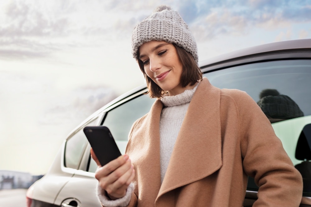 O persoană în palton și căciulă folosește un telefon mobil lângă un vehicul Ford.