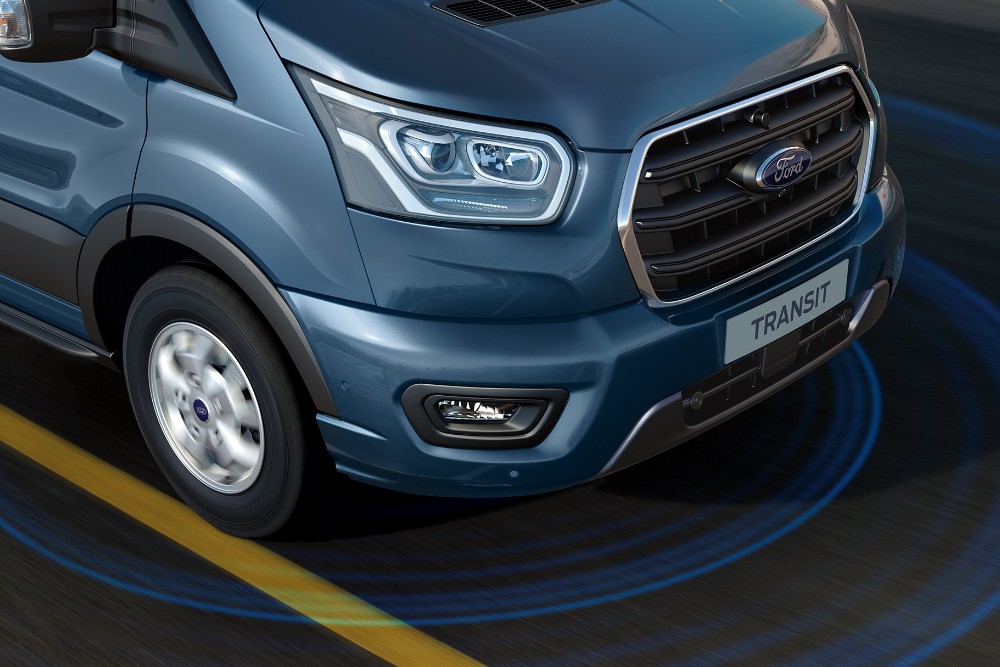Front corner view of a blue Ford Transit van, with parking sensor rings visible on the ground.