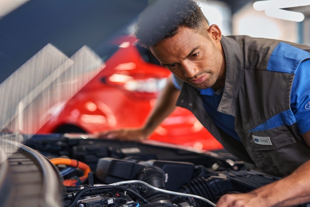 Un tehnician examinează atent motorul deschis al unui vehicul Ford într-un atelier de service.